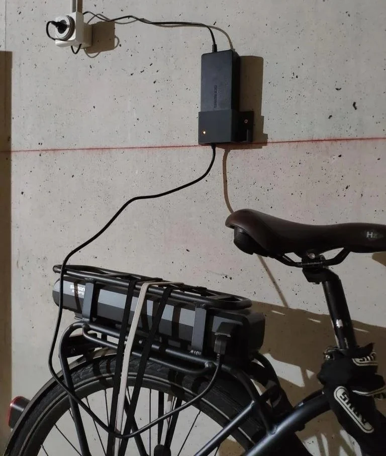 Electric bicycle parked against a wall with a mounted battery and a red laser line running across the wall.