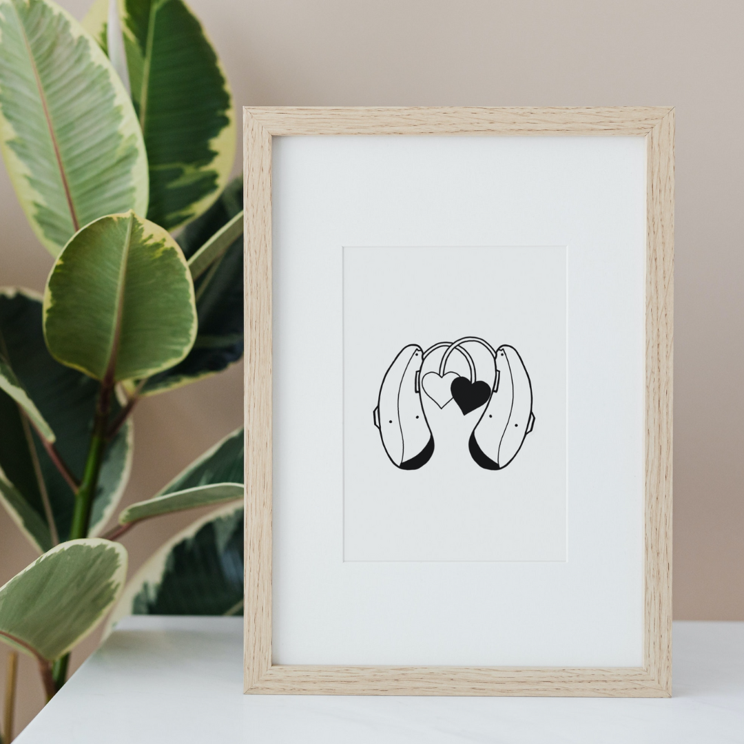 Framed black and white line art illustration of headphones with two hearts hanging from the headphone cords, placed on a white surface next to a green leafy plant.