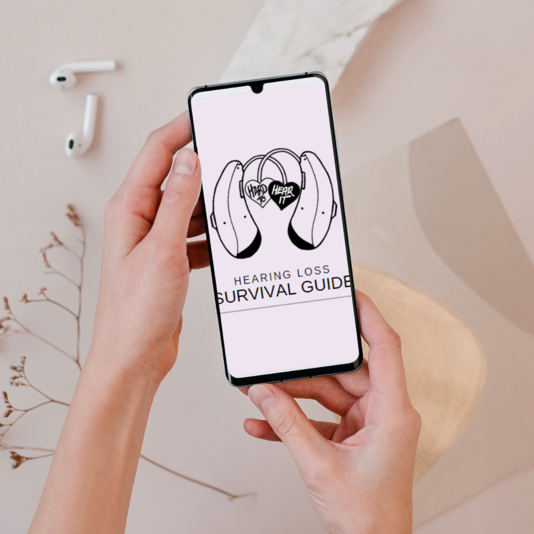 Person holding a smartphone displaying a hearing loss survival guide with an illustration of headphones and a heart with "Hear it" and "Happy" written on it