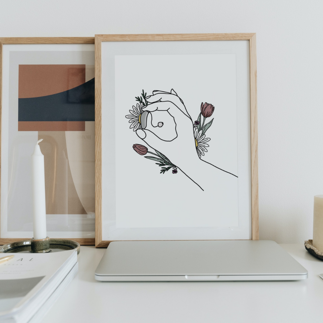 Minimalist desk with framed artwork, candle, laptop, and book.