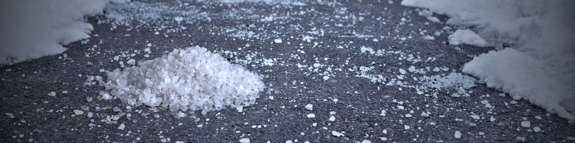 Pile of coarse white salt on a dark asphalt road with overhanging snow on both sides.