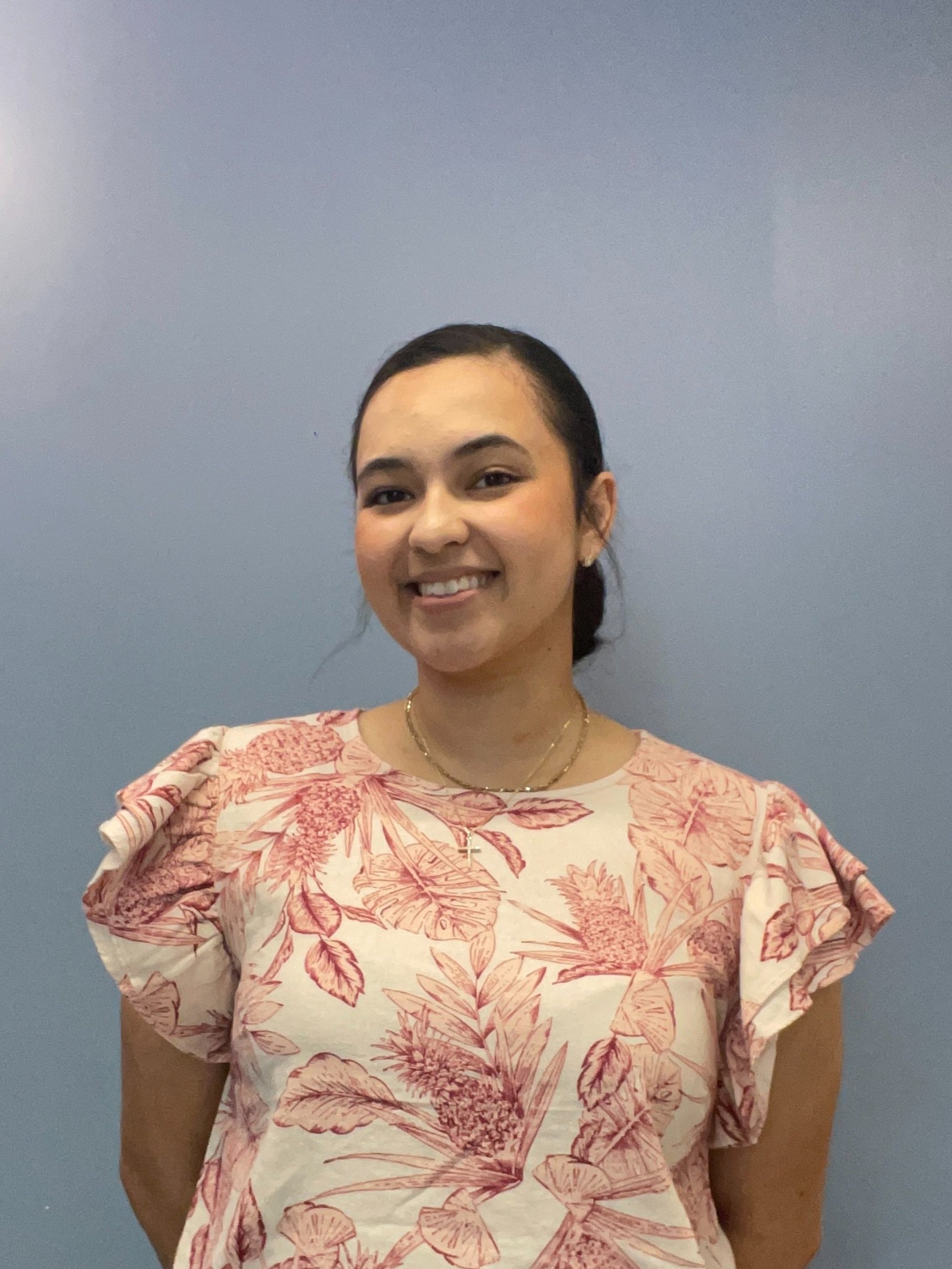 Person wearing a floral-patterned blouse smiling against a blue background