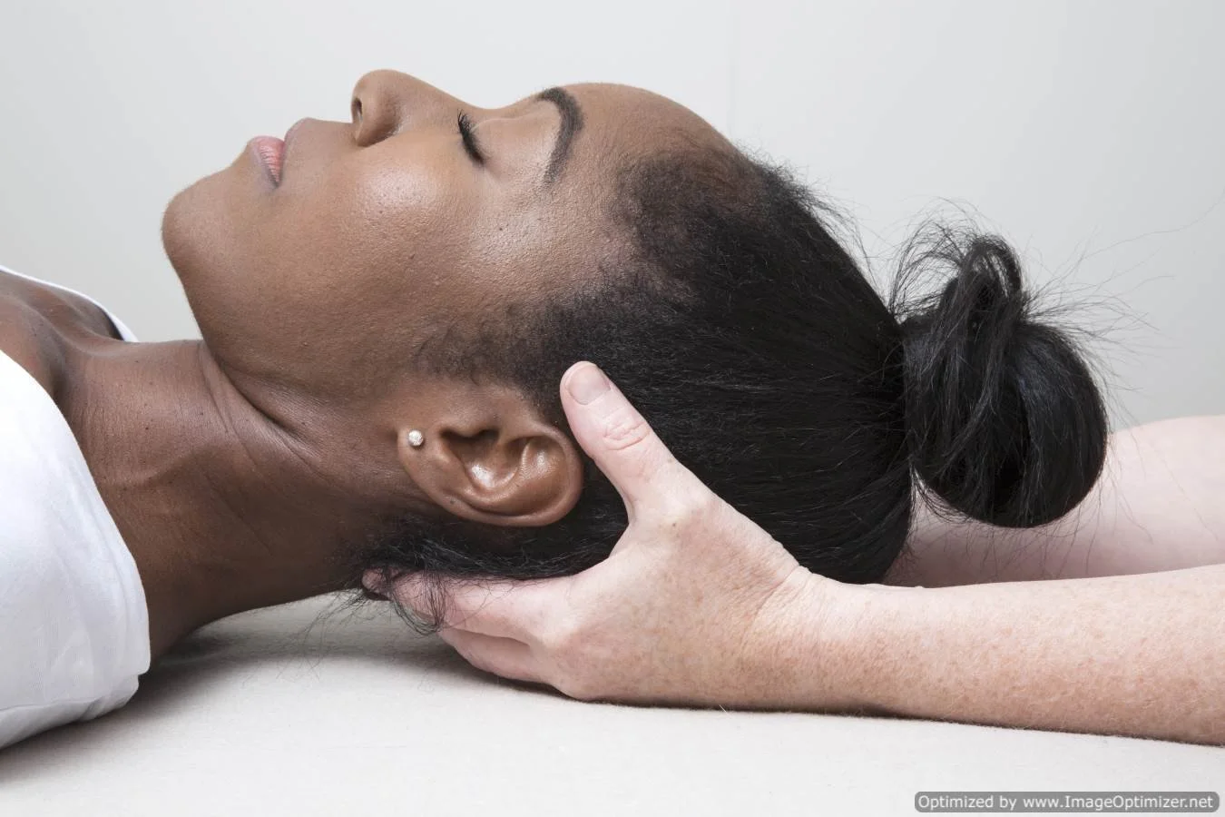 A woman receiving a neck massage while lying on her back with eyes closed, hair styled in a bun.