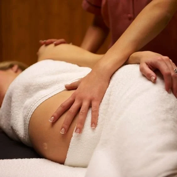 Person receiving a massage, lying on a table covered with a white towel, with the masseuse's hands on their back.