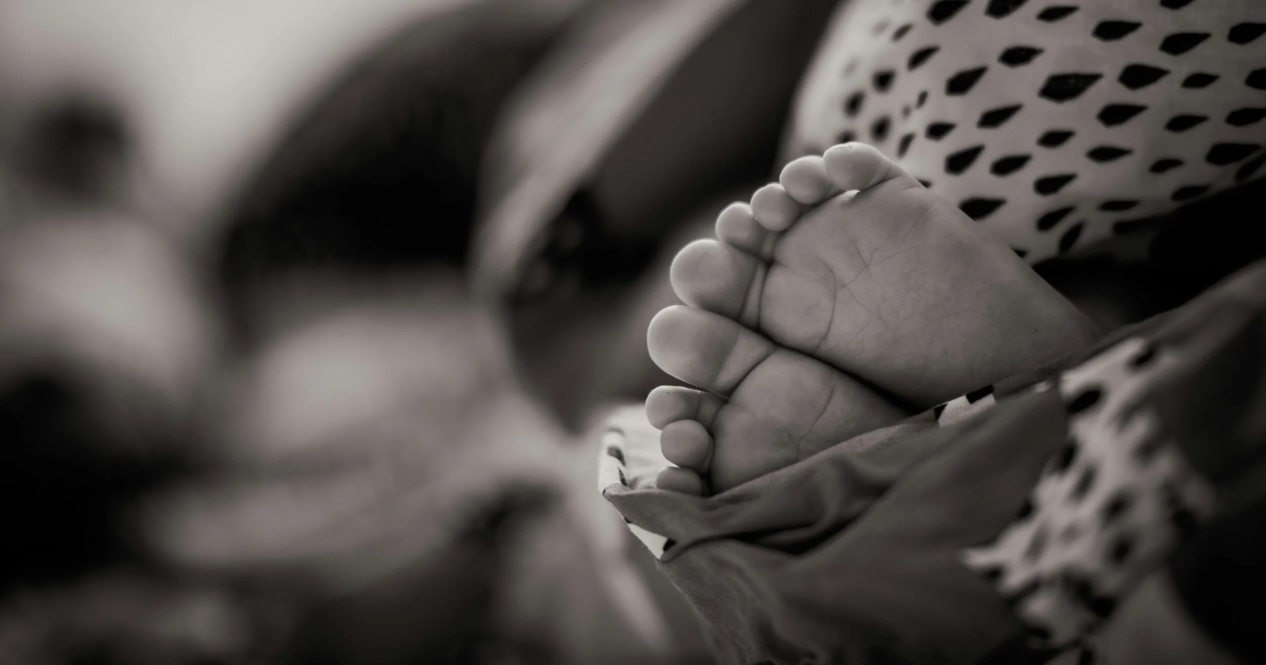 Close-up of a newborn baby's feet, showing tiny toes and cracked soles, wrapped in a patterned blanket.