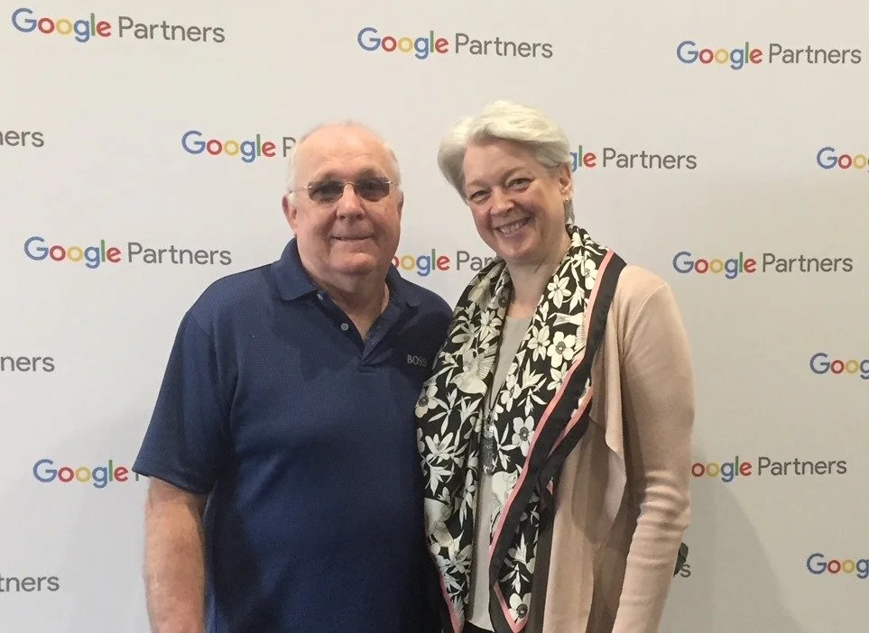 Two people, a man and a woman, smiling and standing together in front of a backdrop with Google Partners logos.
