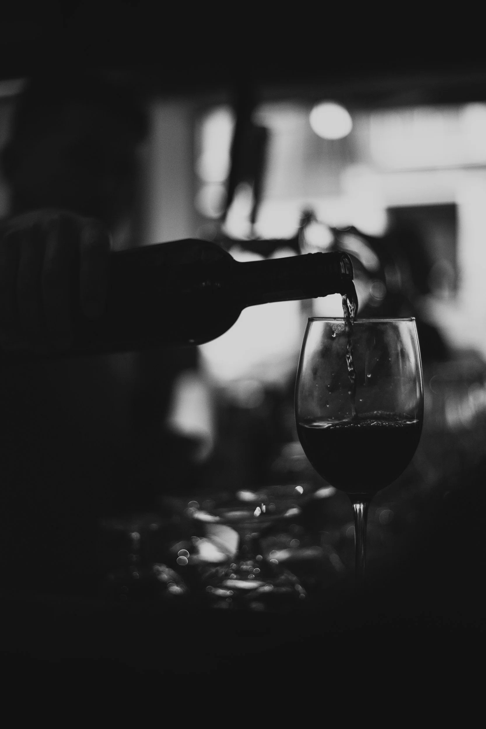 Black and white photo of a bottle pouring wine into a wine glass.