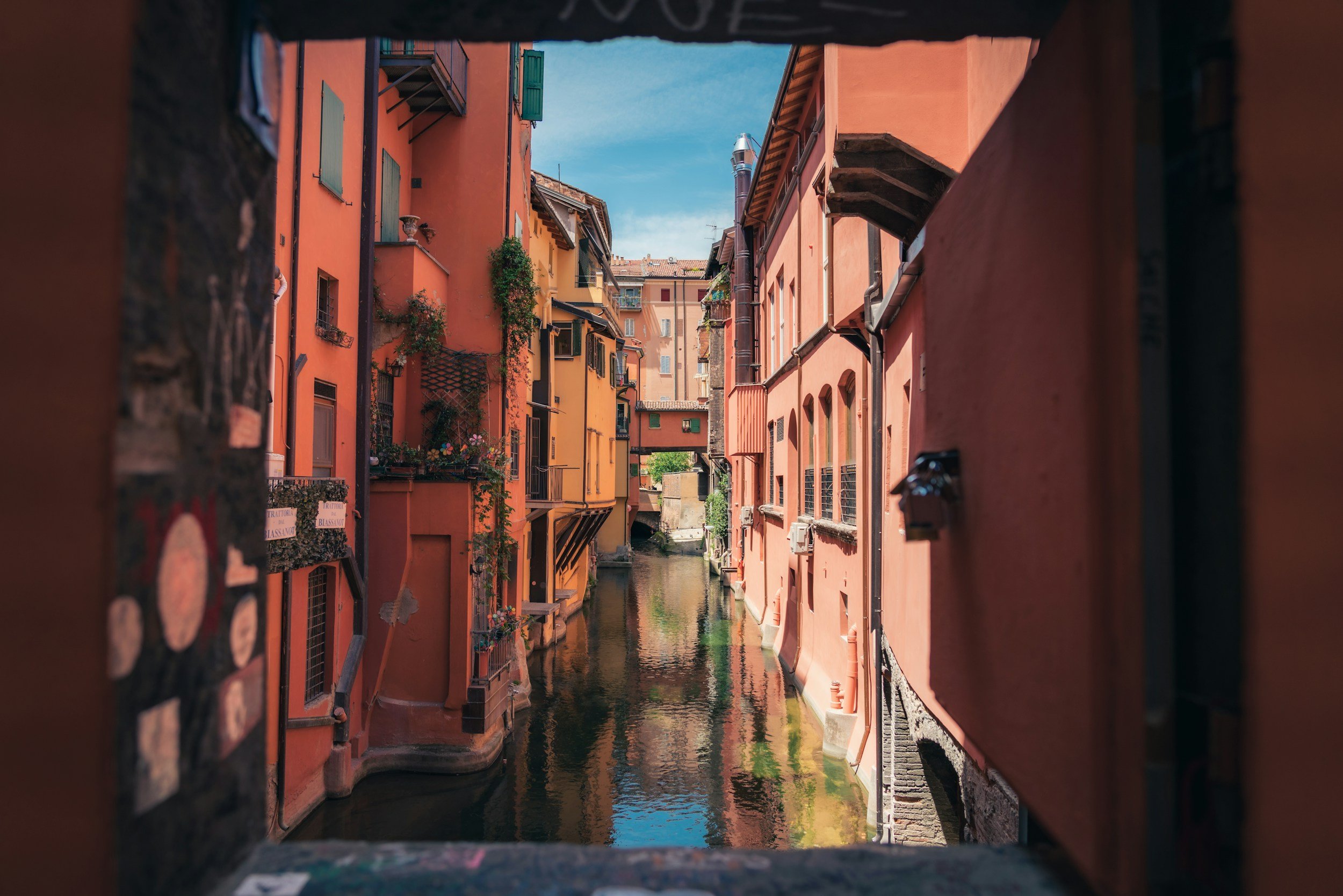 View of colorful buildings along a canal, taken through a small square opening in a wall.