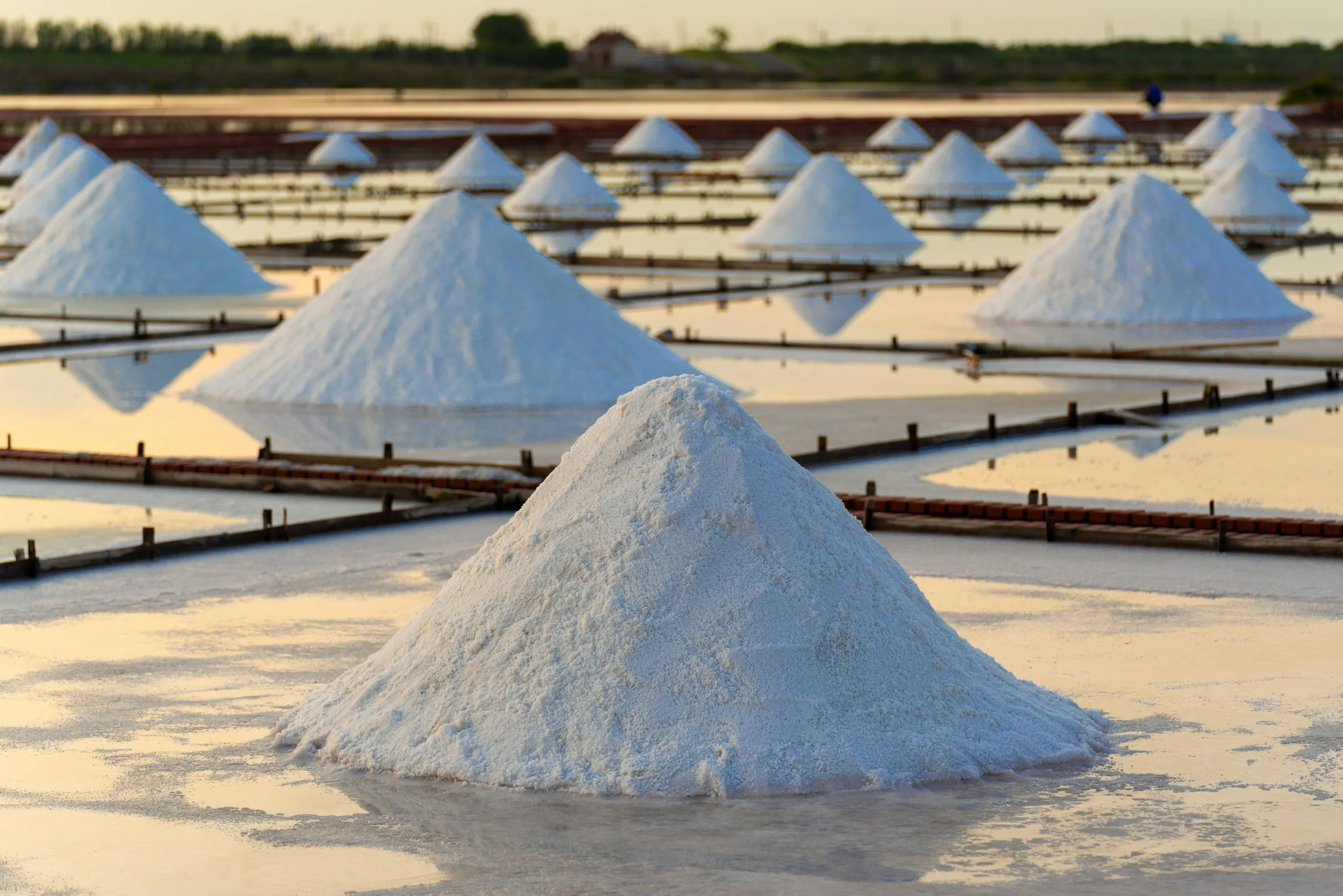 Salt piles on salt evaporation ponds during sunset with pink and orange sky.