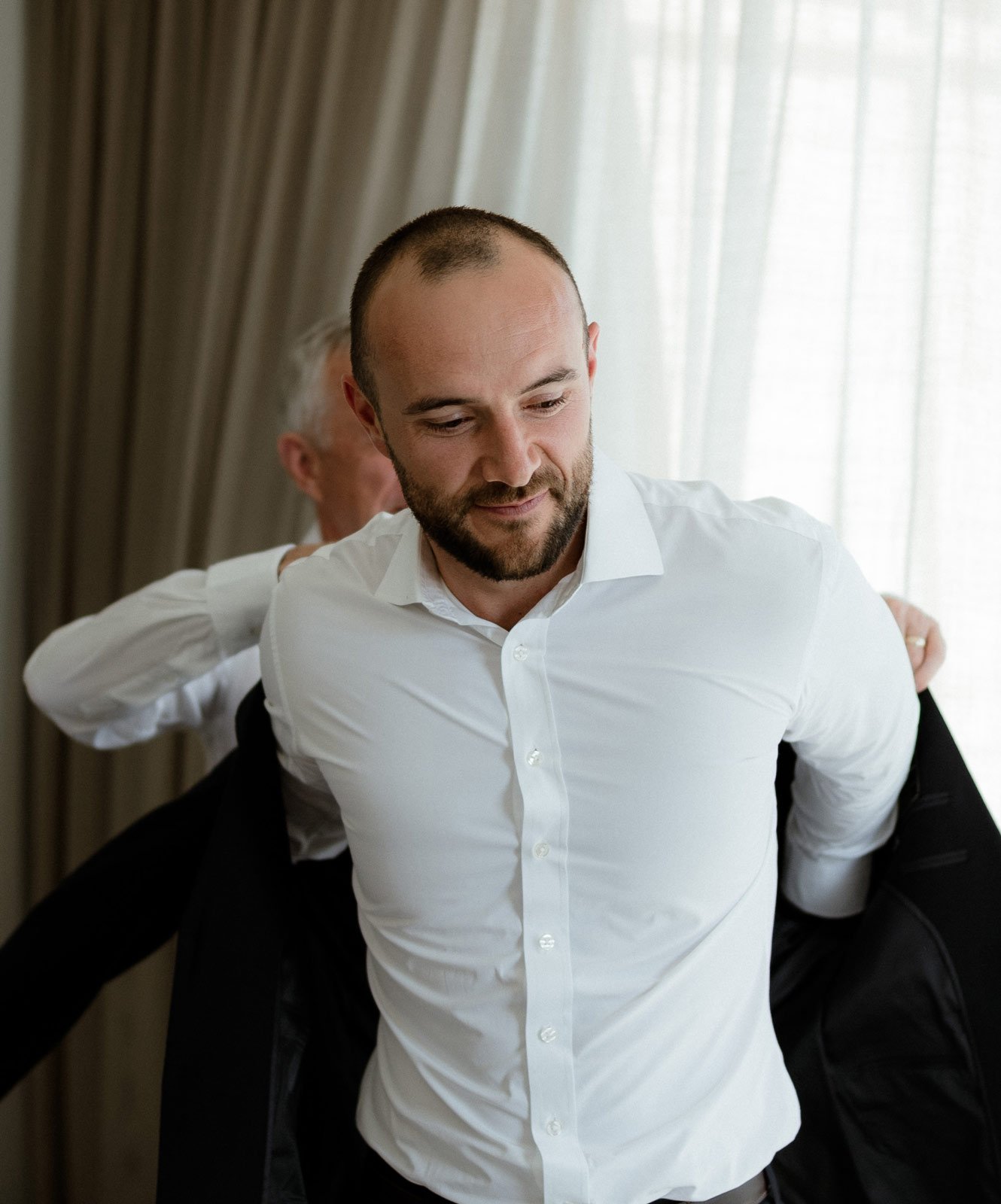 father of the groom helping his son put on his wedding suit