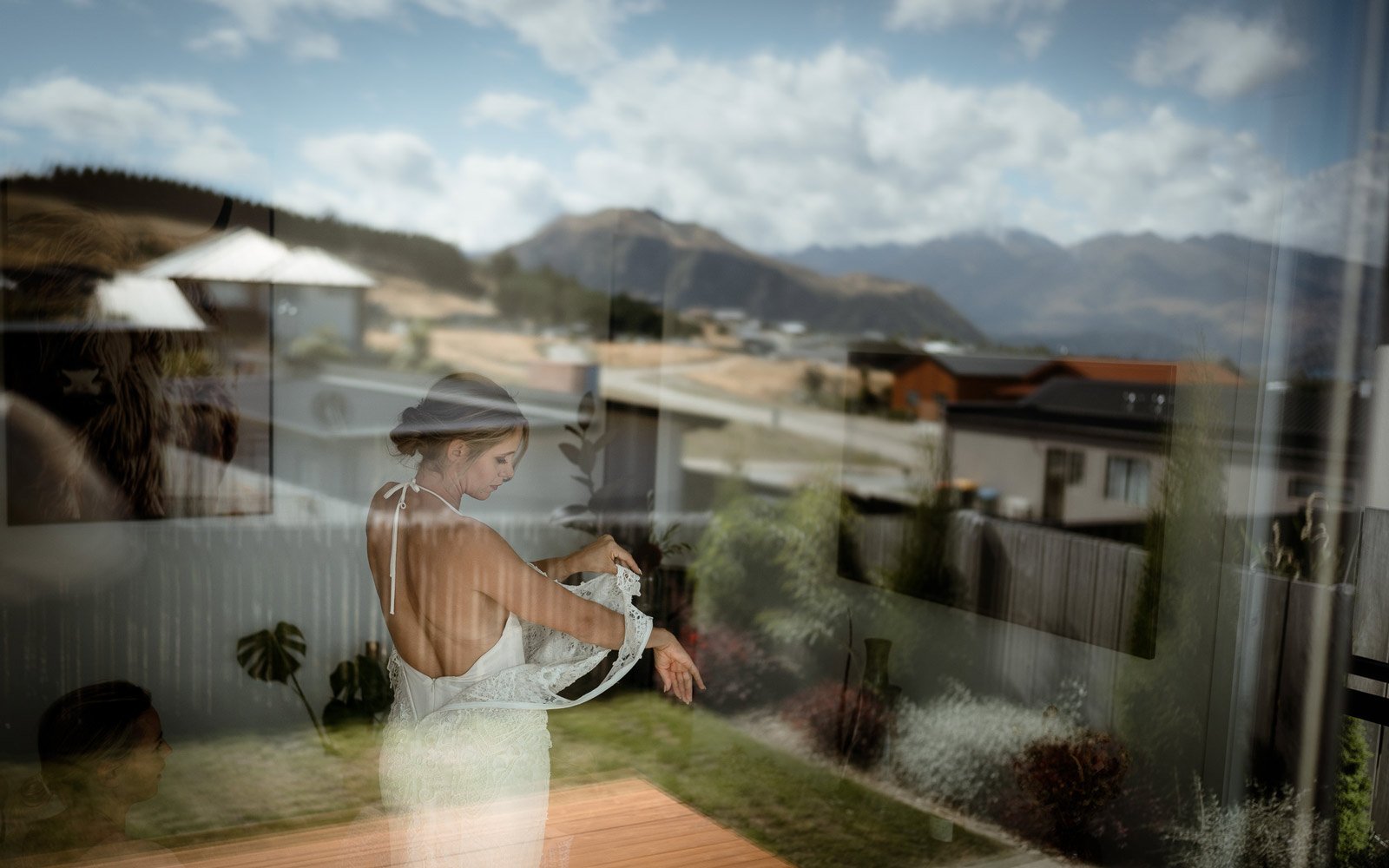 bride getting into her stunning wedding dress, reflection of the mountains in the window