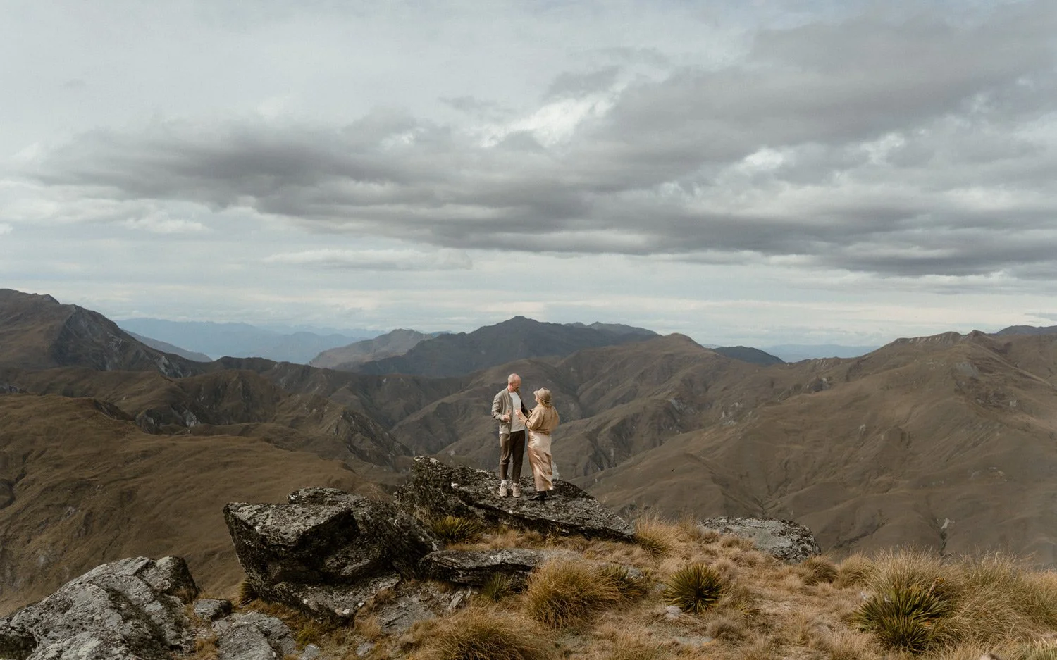 Elopement couple reading vows at their Queenstown heli wedding on Vanguard Peak. Views of the Southern Alps mountains and tussock in the background. 