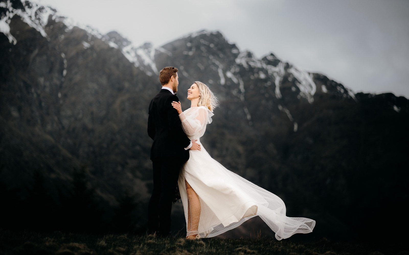 couple embrace at the foot of the Remarkables with the brides wedding dress blowing in the cool wintery queenstown breeze
