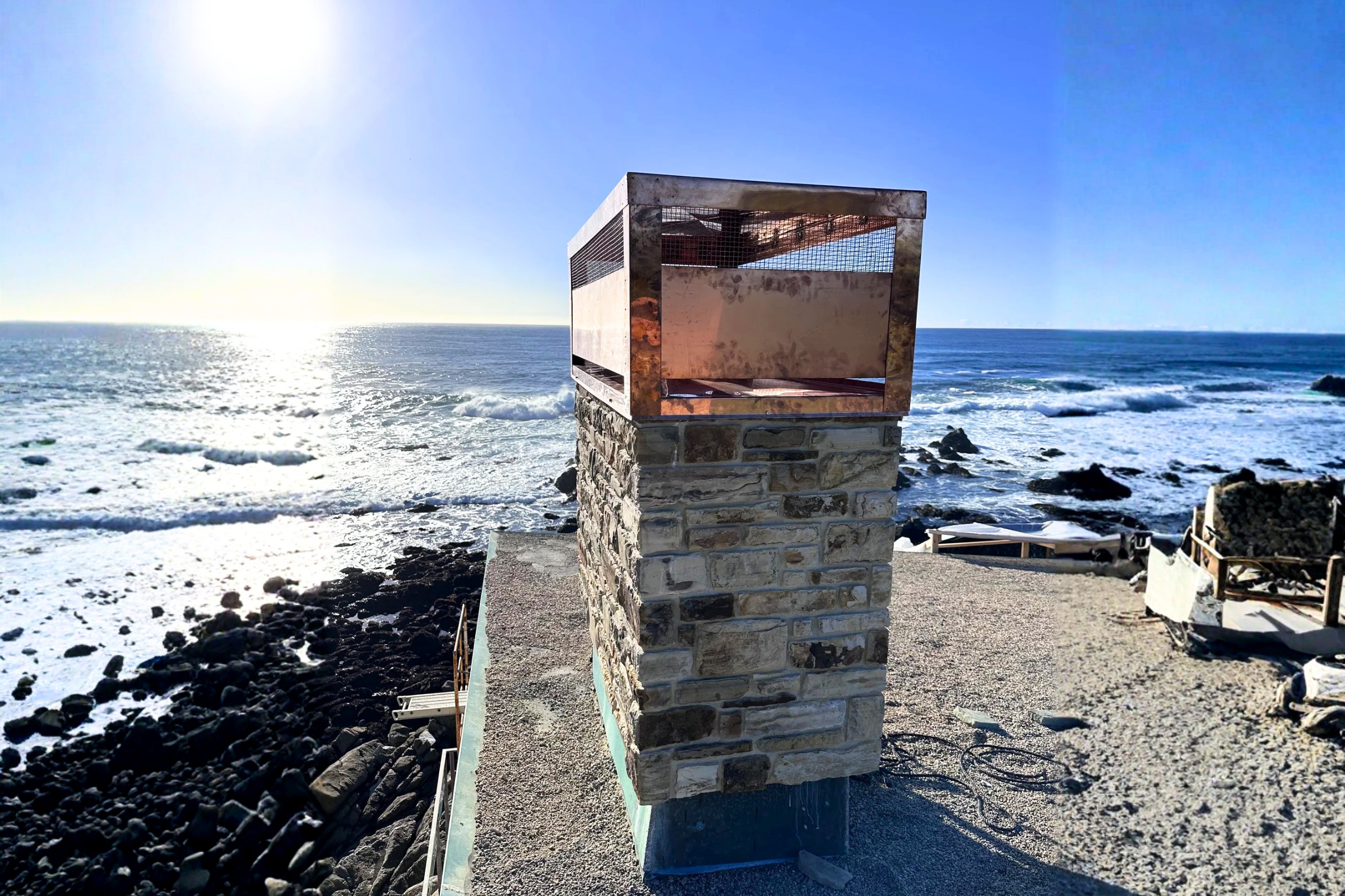 Custom sheet metal chimney cap fabricated and installed on a coastal stone chimney in Carmel Valley California