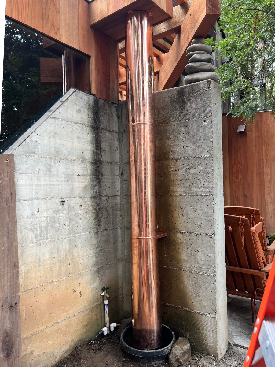 Custom copper downspout installed beside a concrete wall