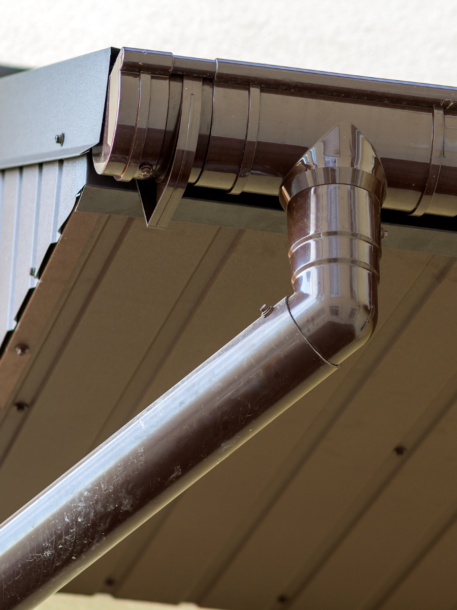 Brown metal gutter and downspout installed beneath a residential roof