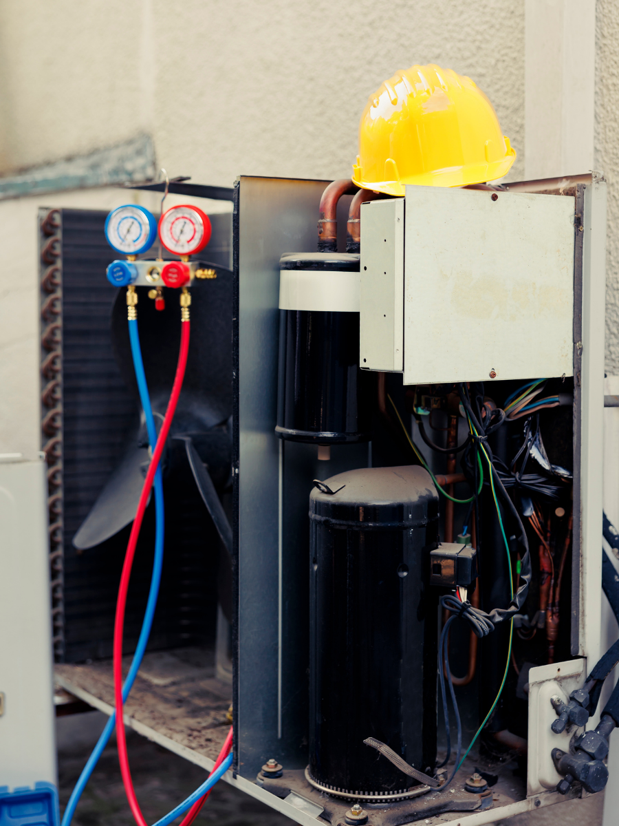 Open outdoor HVAC unit connected to diagnostic refrigerant gauges