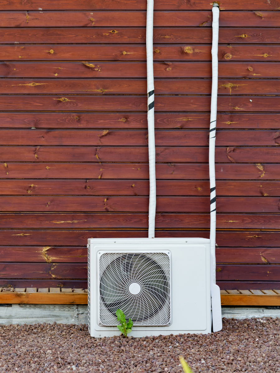 Outdoor ductless mini-split condenser installed beside a wood-sided home