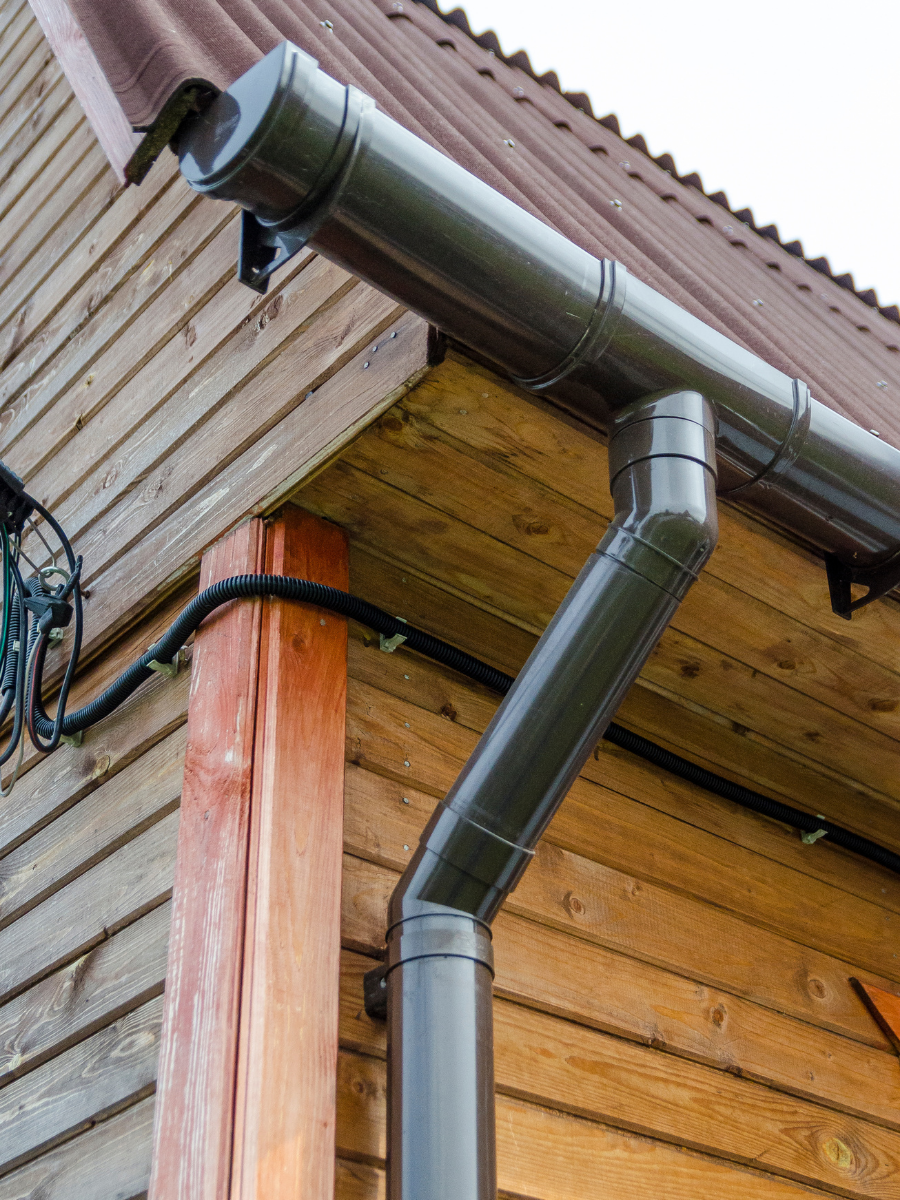 Dark metal gutter and downspout installed on a wood-sided home