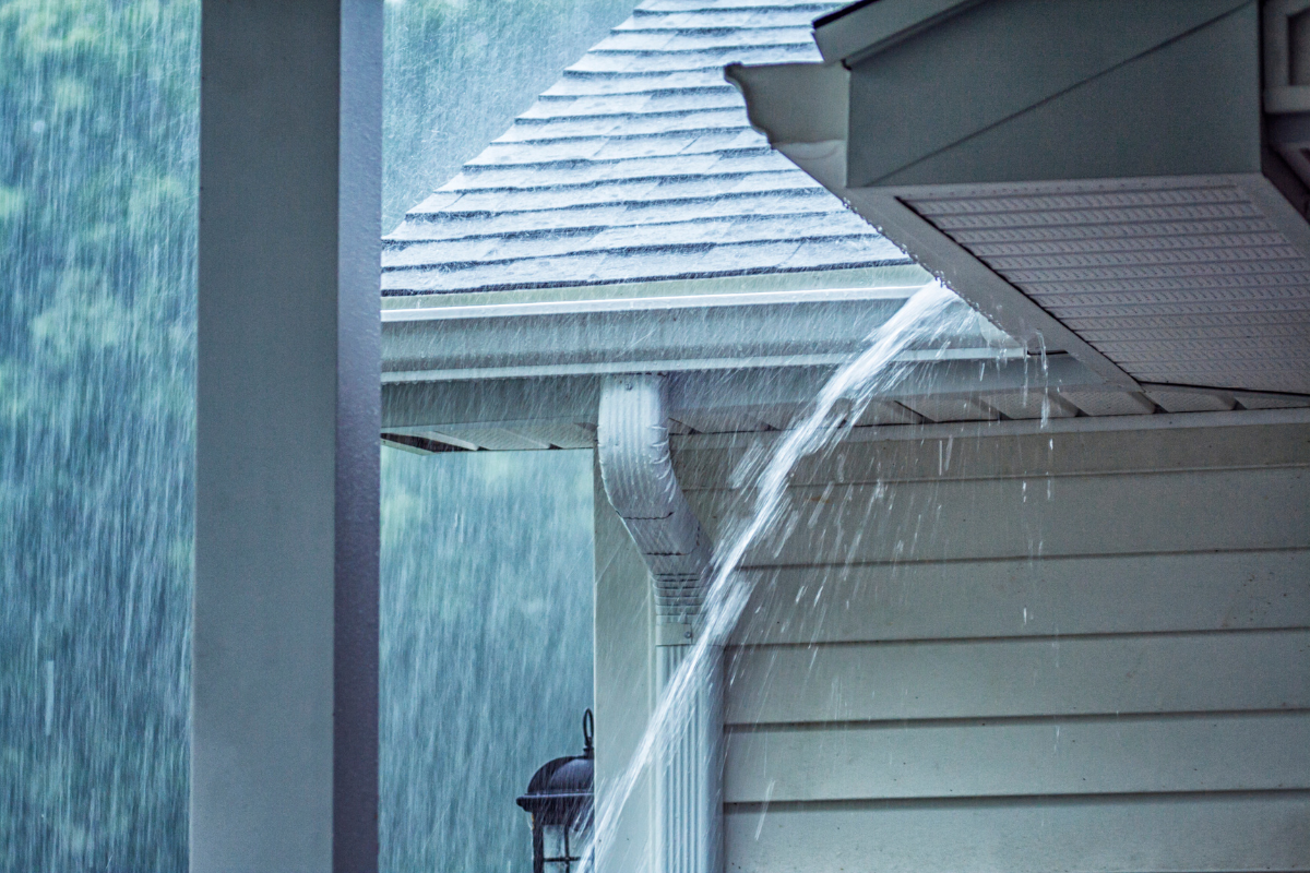 Rainwater overflowing from a residential roof gutter during heavy rain, showing a possible drainage problem.