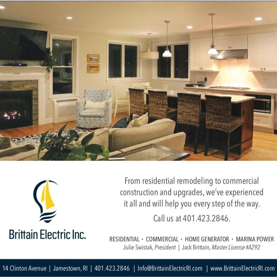 Living room with fireplace, armchair, sofa, kitchen island with barstools, and hanging pendant lights.