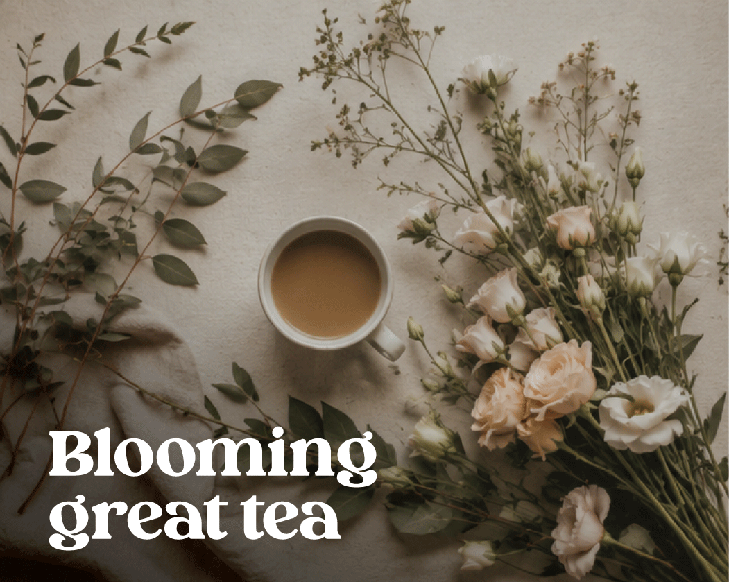 A cup of tea placed on a white surface next to a bouquet of light-colored flowers and green leaves.