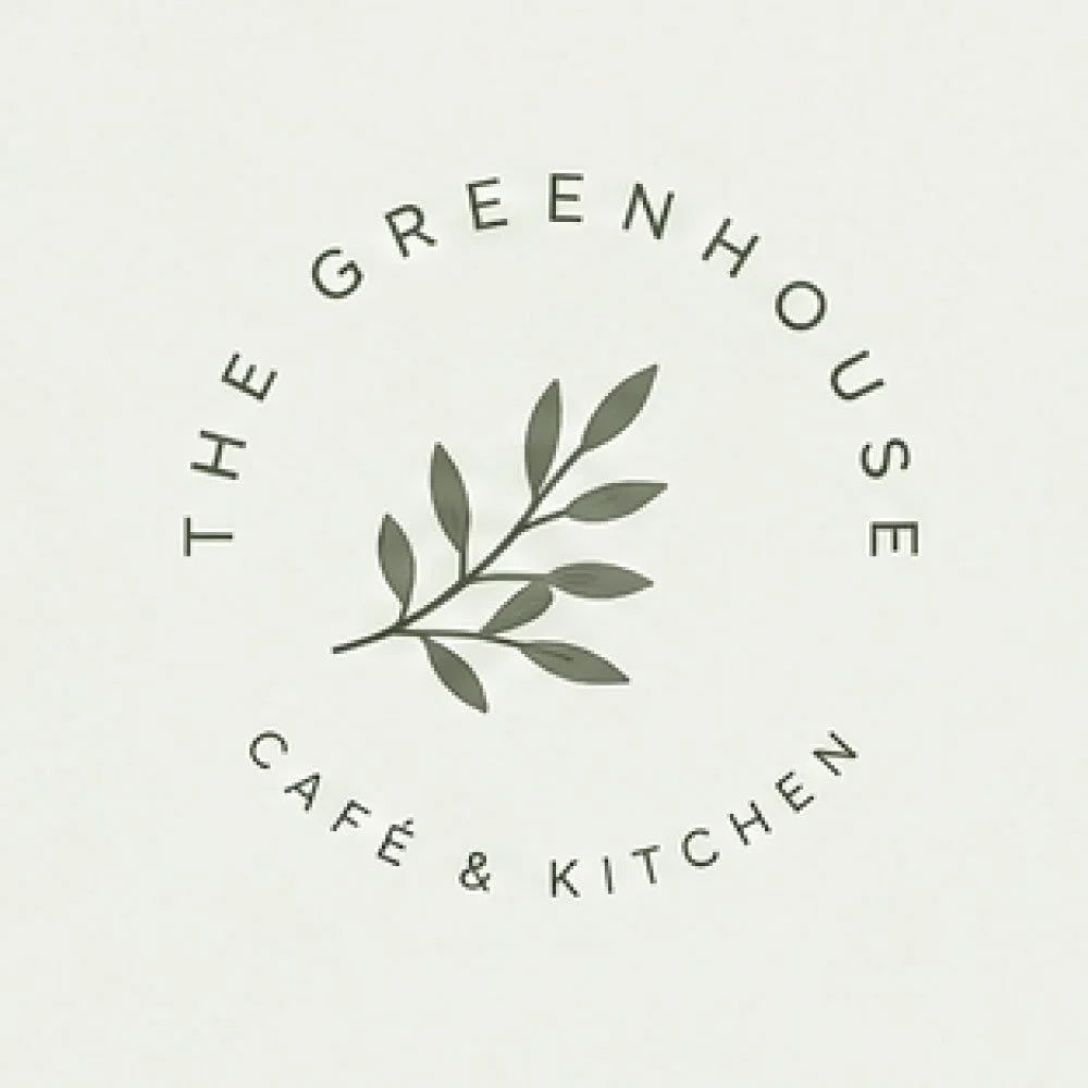 Logo of The Greenhouse Cafe & Kitchen featuring a circular design with a central illustration of a gray leafy branch.