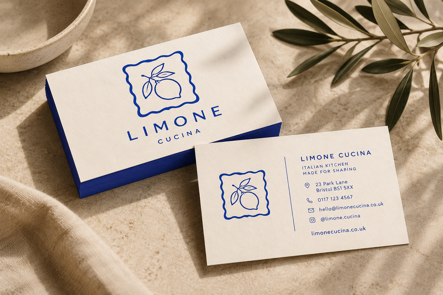 Business cards for Limone Cucina, an Italian restaurant, placed on a textured surface with some green leaves nearby.