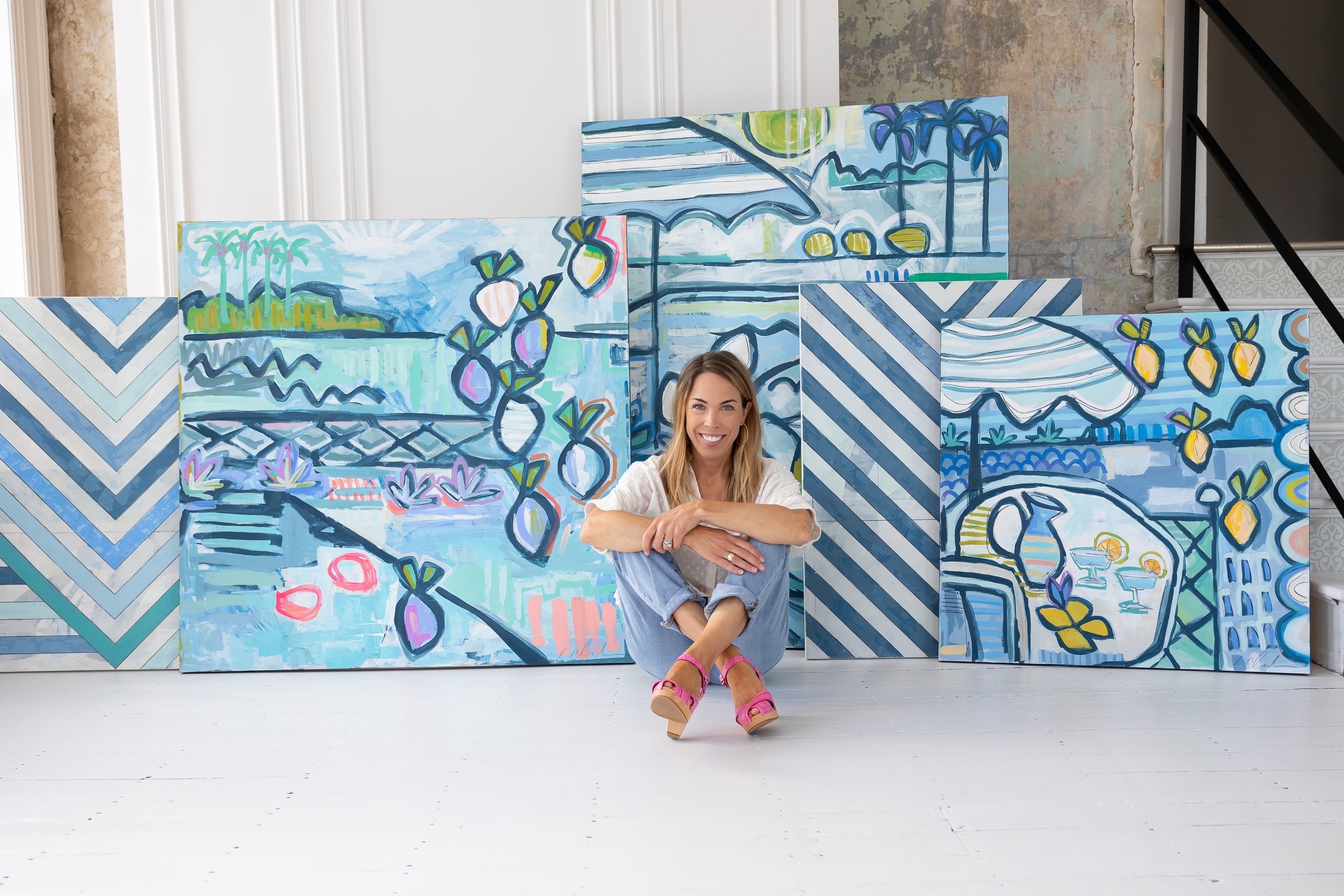 Erin Clark sitting in front of her abstract landscape paintings.