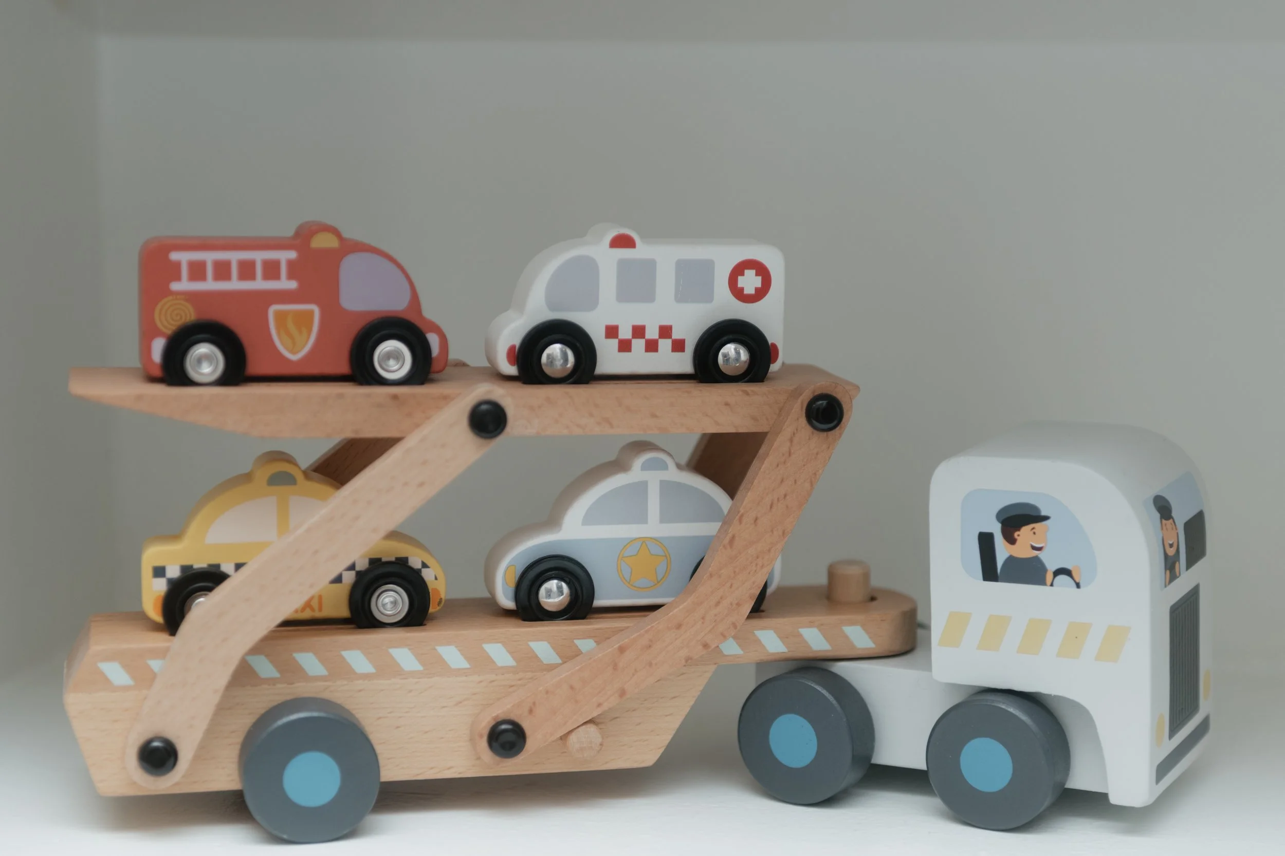 Collection of small wooden toy vehicles, including fire trucks, ambulances, and taxis, displayed on a wooden shelf.