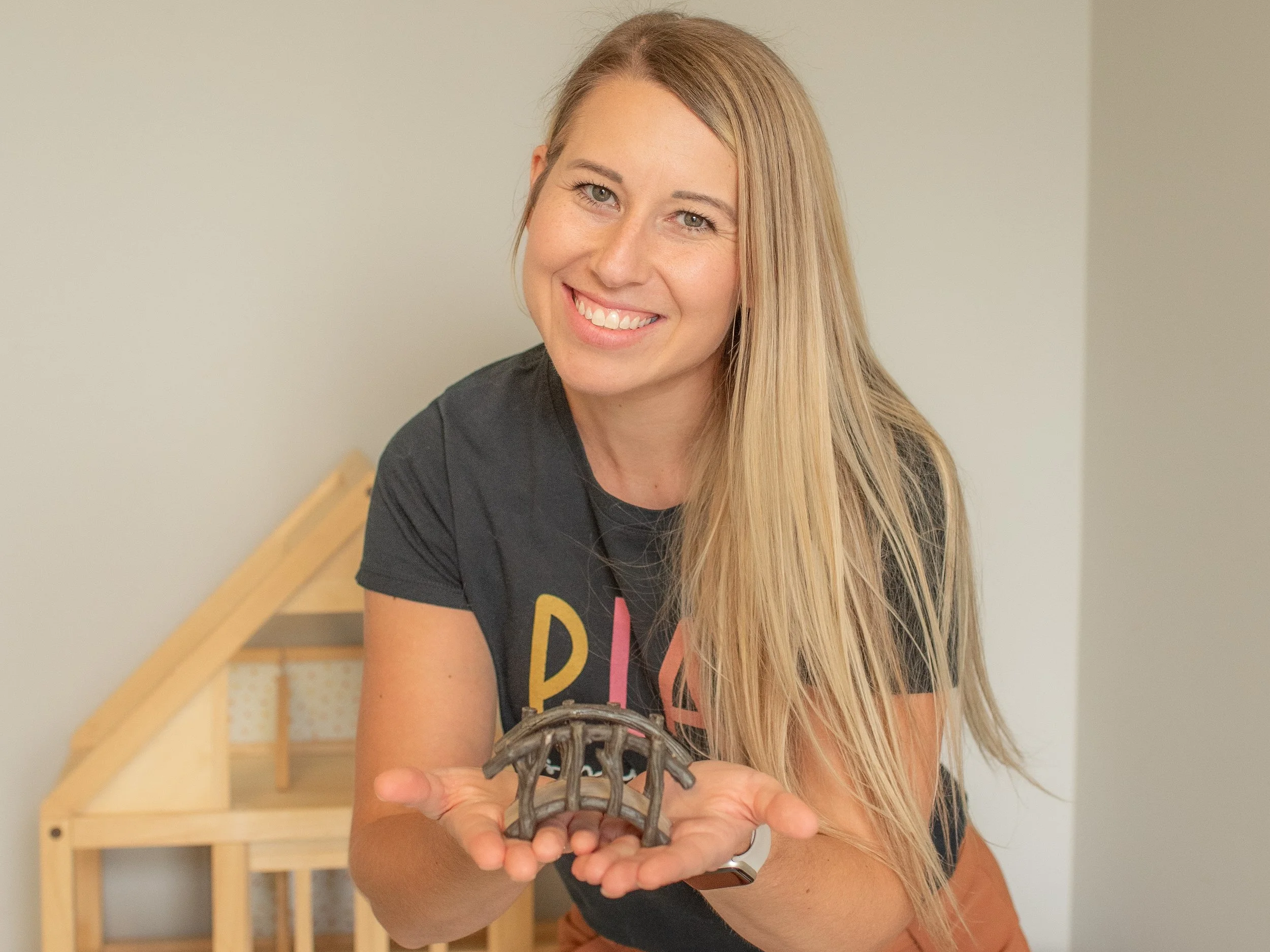 A smiling woman with long blonde hair holding a small, gray, metallic object in her hands.