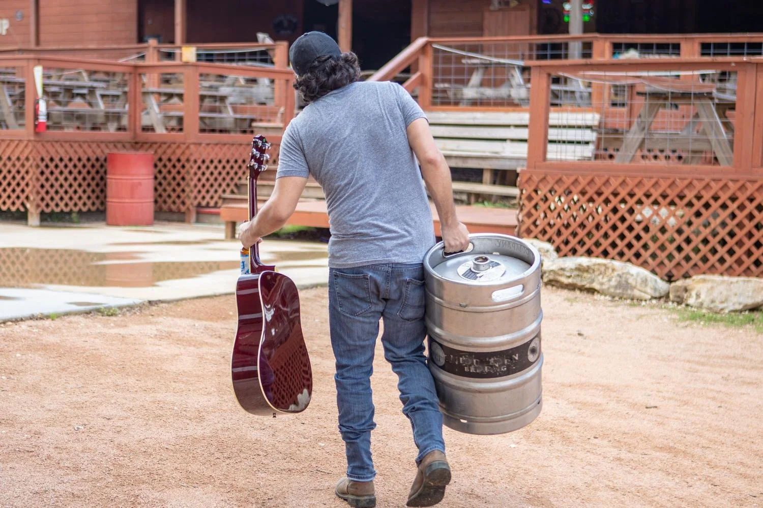 Jeff jacobs from the back walking away holding a keg in one hand and his guitar in another outdoors