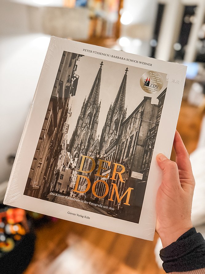 A person holding a book titled "Der Dom" with a black-and-white photo of a cathedral on the cover.