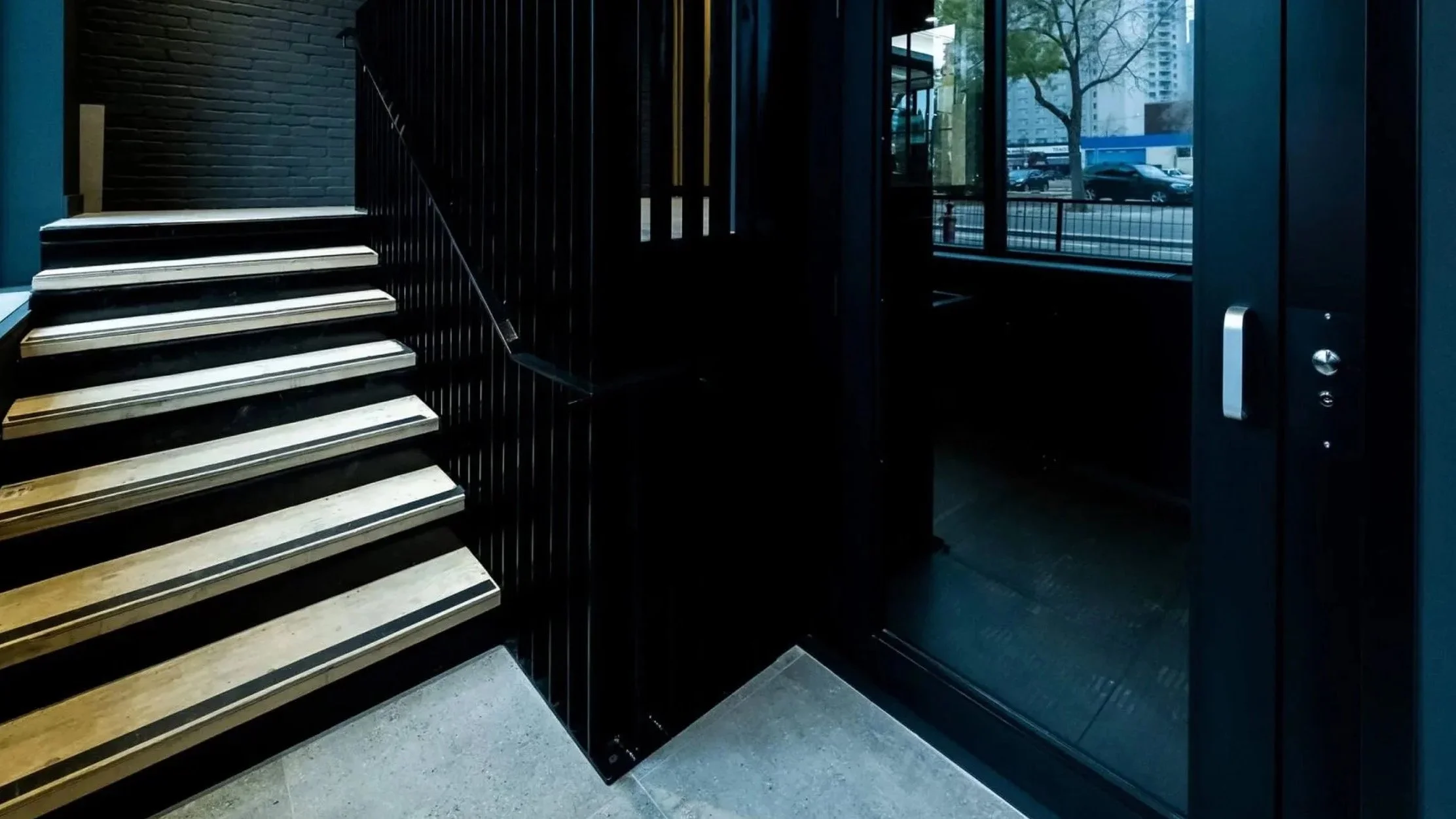 Butler Mobility - RAM Stratus Elevator in a modern commercial building with sleek black interior and and ivory staircase to the left
