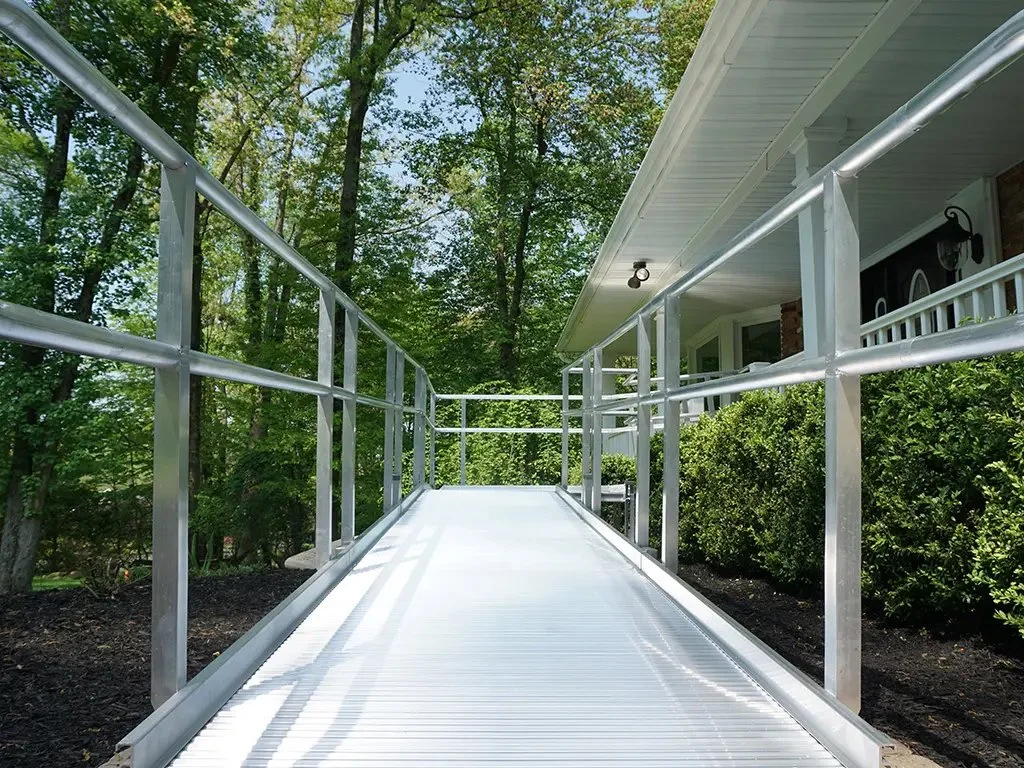 An aluminum Butler Mobility wheelchair accessible ramp outside surrounded by bushes and trees.
