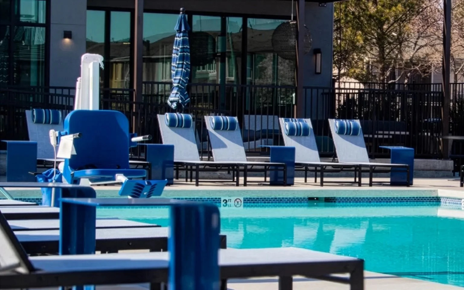 A commercial hotel featuring a Butler Mobility Aquacreek Ranger 2 accessible pool lift with a blue seat next to a pool and pool side chairs