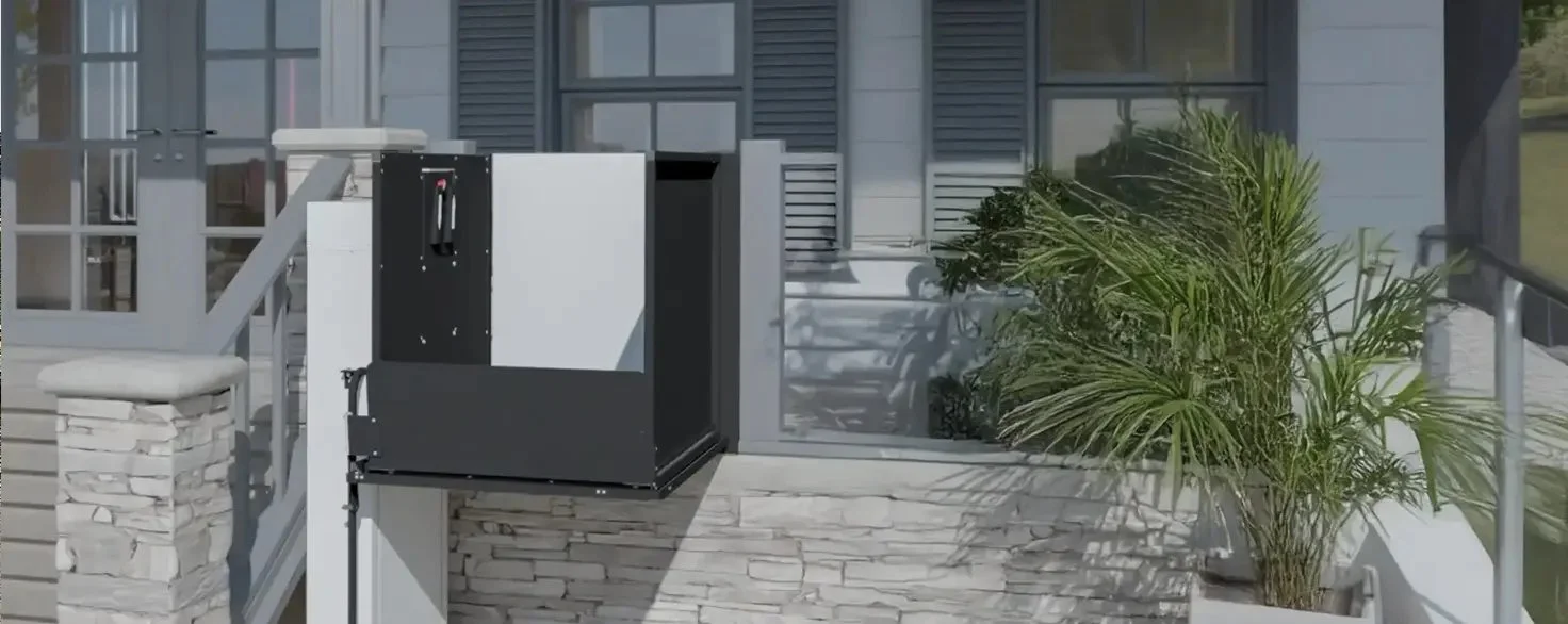 A Butler Mobility - RAM vertical platform lift attached to a residential porch next to a staircase, home is white with grey shutters