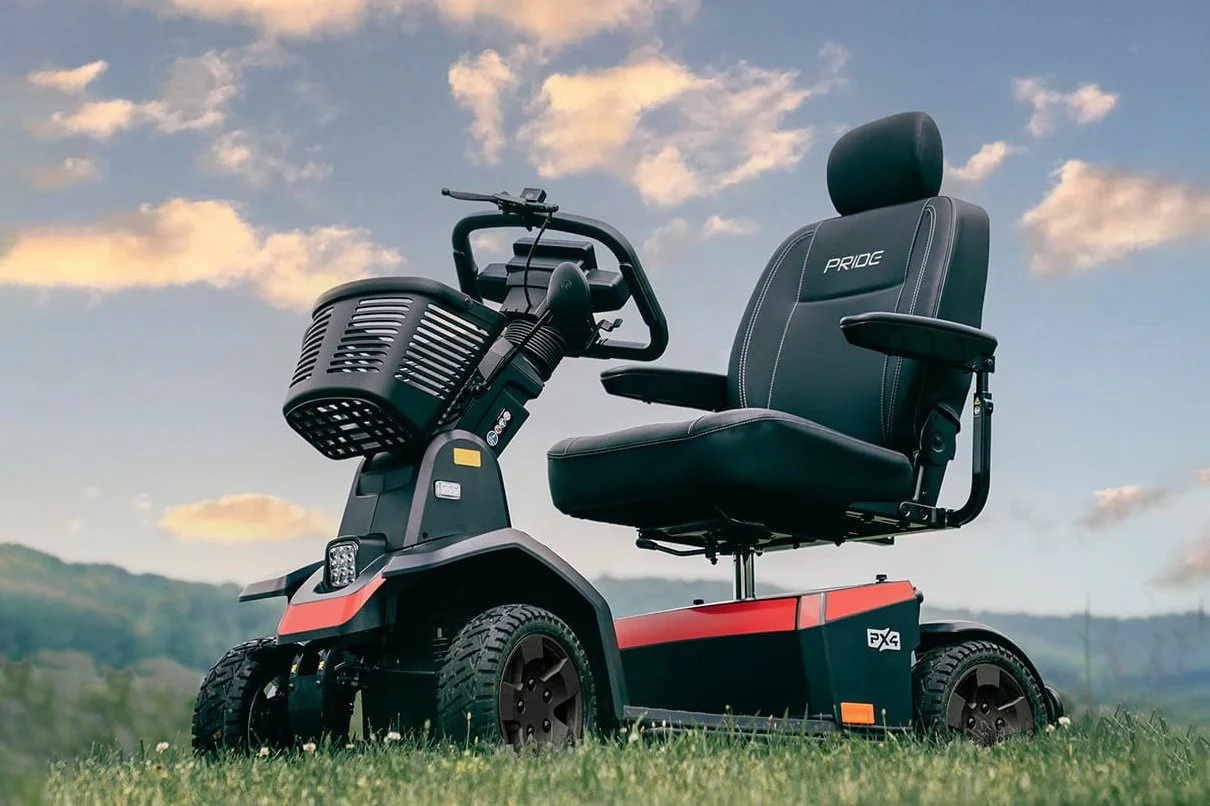 A Pride Mobility PX4 heavy-duty 4-wheel mobility scooter parked on green grass against a cloudy sunset sky.