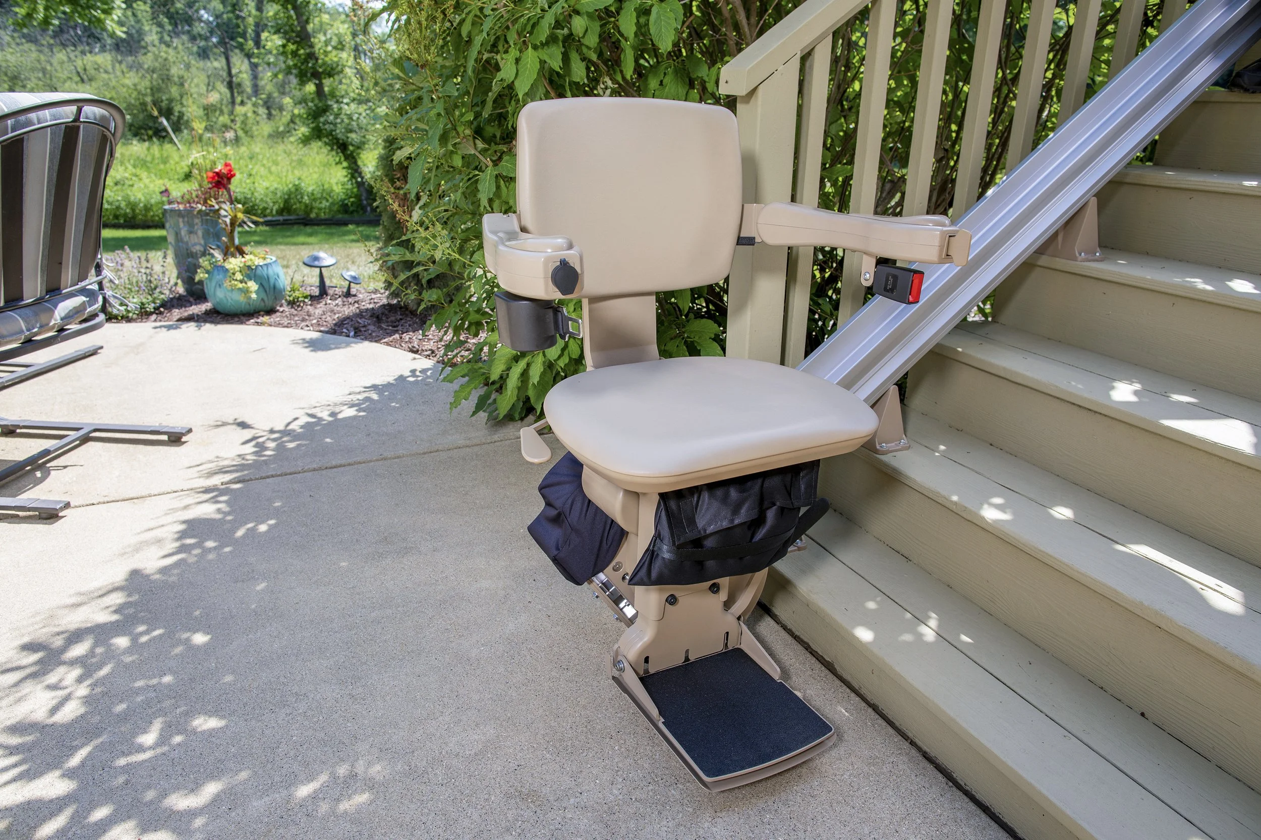 A Butler Mobility Outdoor Straight Stairlift surrounded by green shrubs and grey wooden staircase