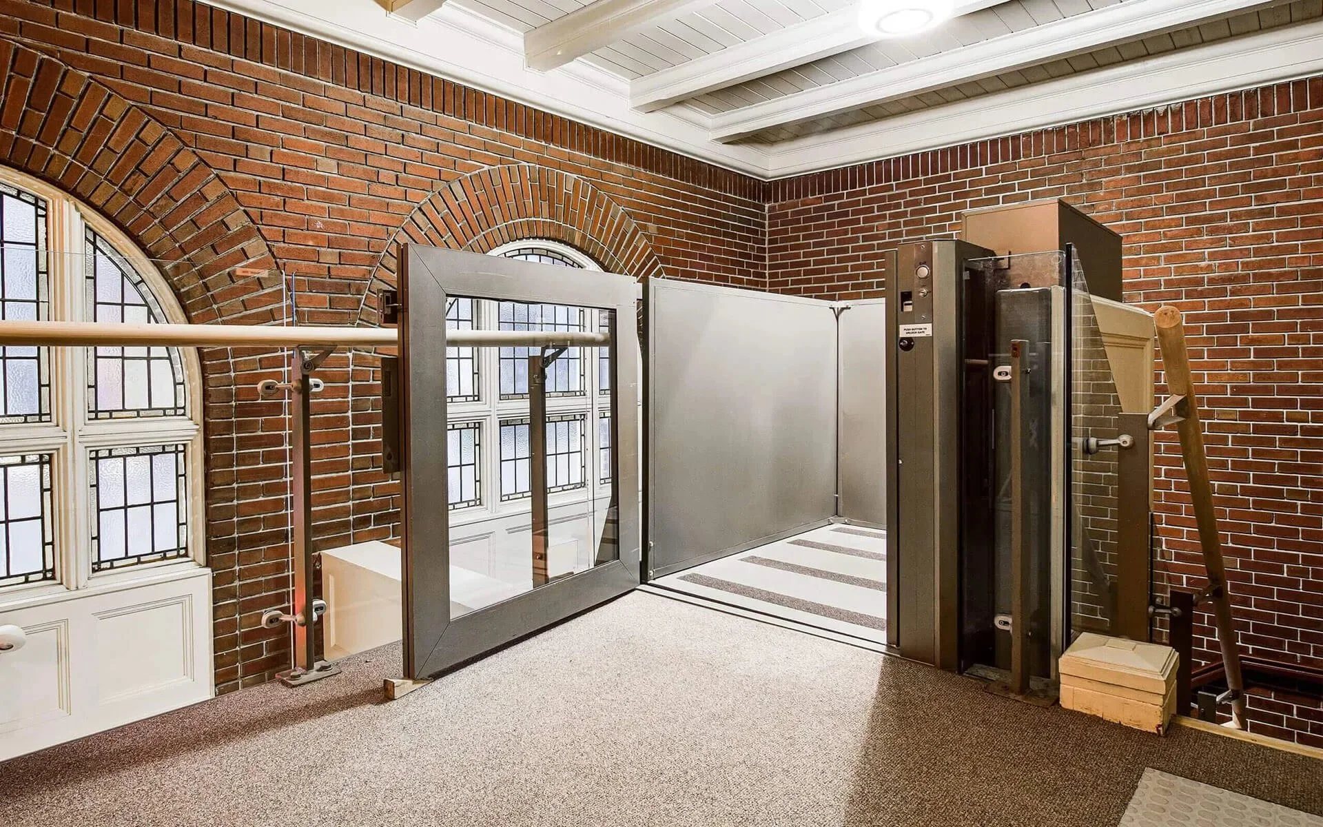 A Butler Mobility - RAM Flex vertical platform lift in a commercial building with brick walls