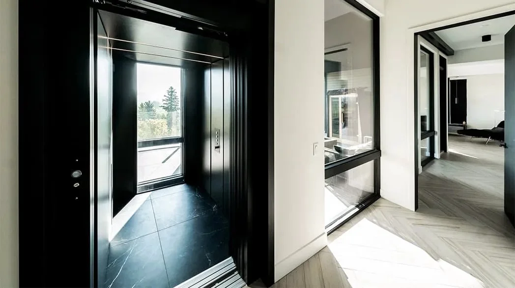 A Butler Mobility - RAM Stratus Elevator in a modern residential home featuring a black interior of the elevator and white wall of home with black trim