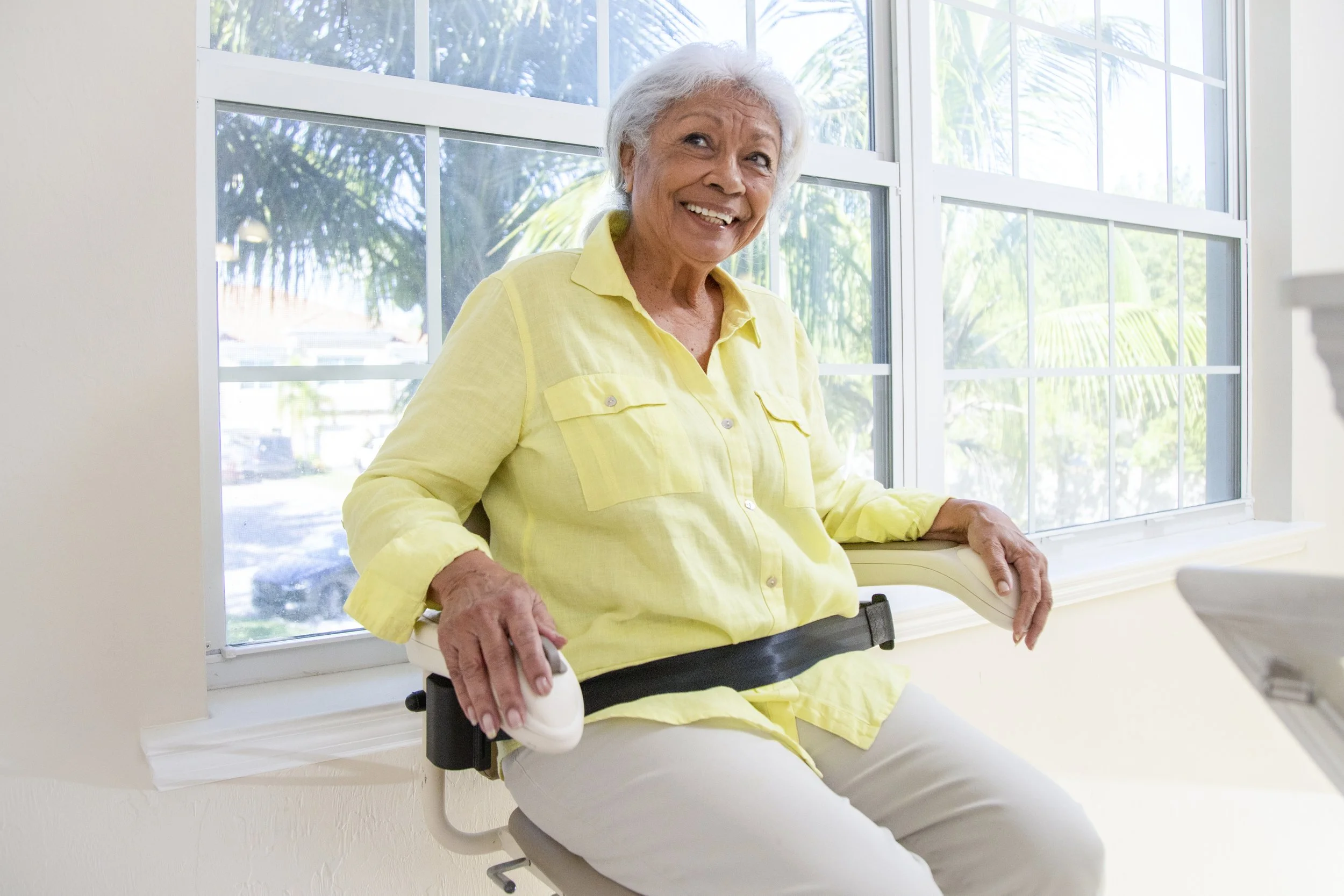 A woman wearing yellow seated in a Butler Mobility Harmar straight stairlift