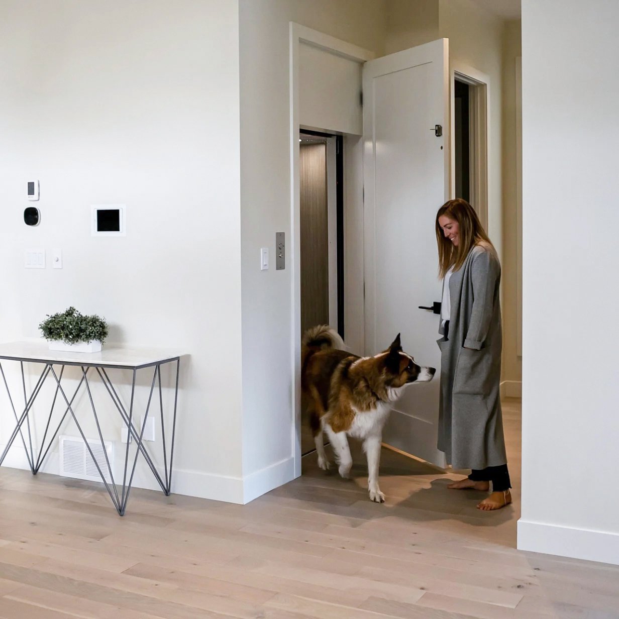 A Butler Mobility - RAM Crystal Elevator  in a residential modern home with white walls, a woman and her dog exit the elevator