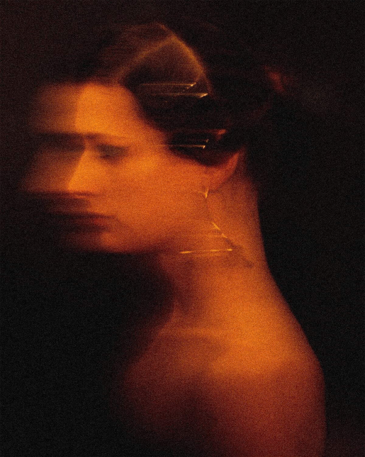 Retrato artístico en tonos cálidos de una mujer con maquillaje oscuro y sombrero de ala ancha, en un ambiente oscuro