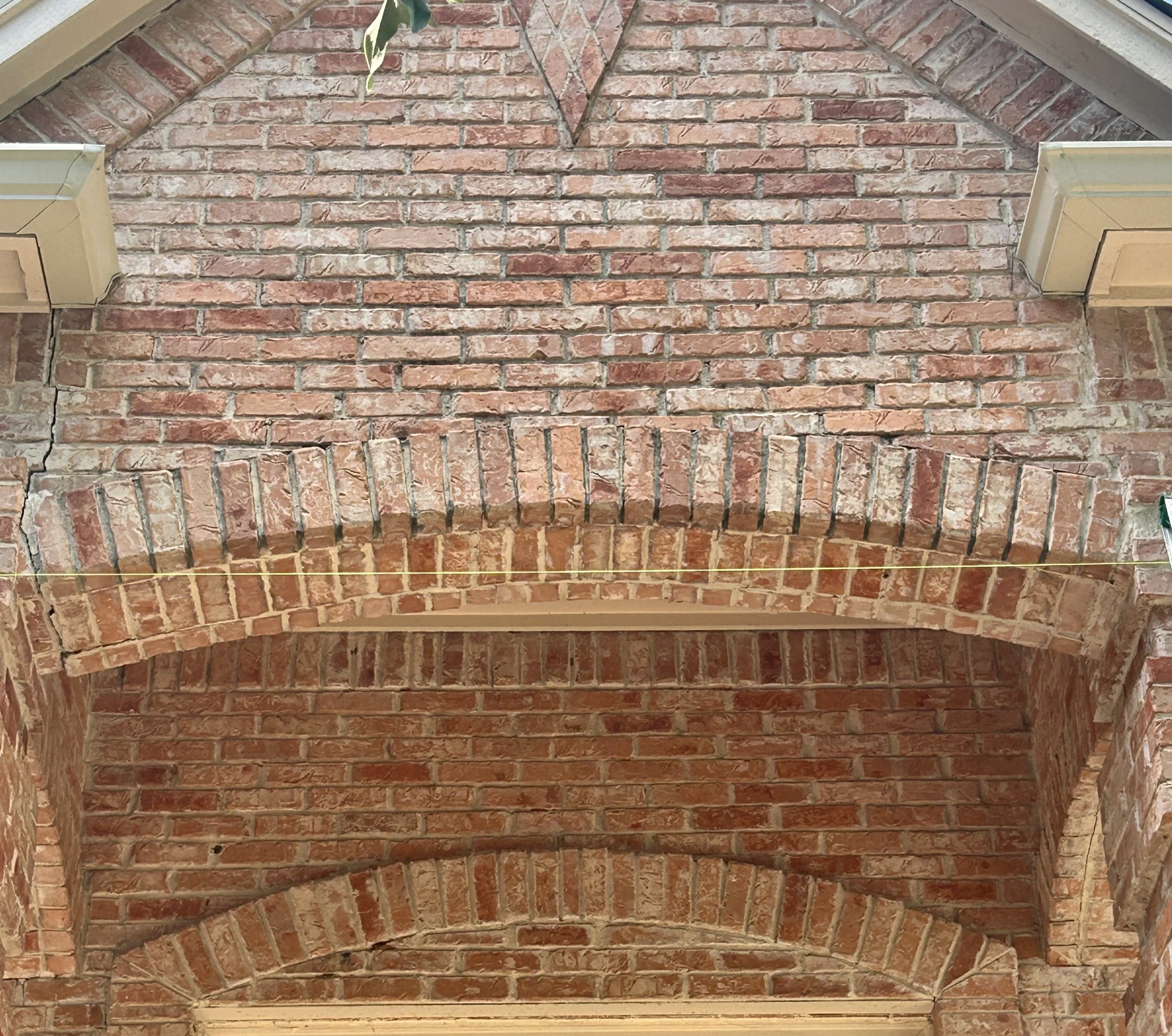 Close-up view of a brick archway with layered brick construction and mortar, with some green leaves hanging overhead.