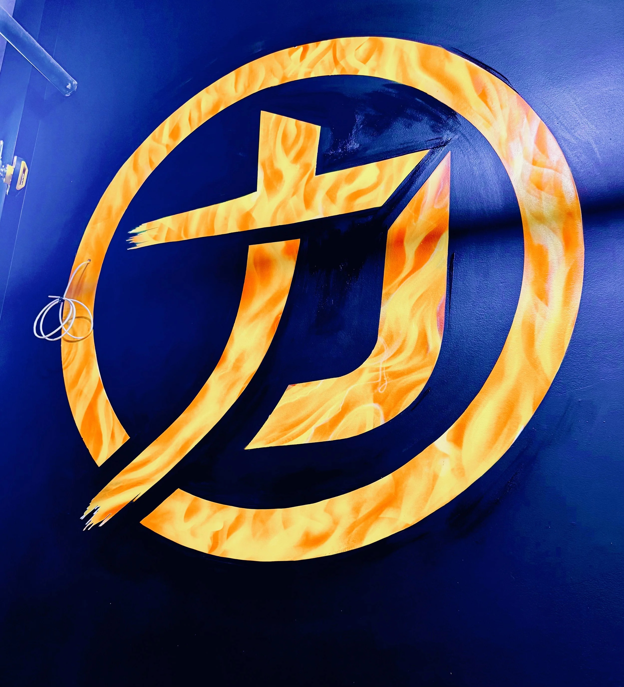 Close-up of a sign with a black background and orange/yellow flame design forming a stylized letter 'G' or 'Q' shape.