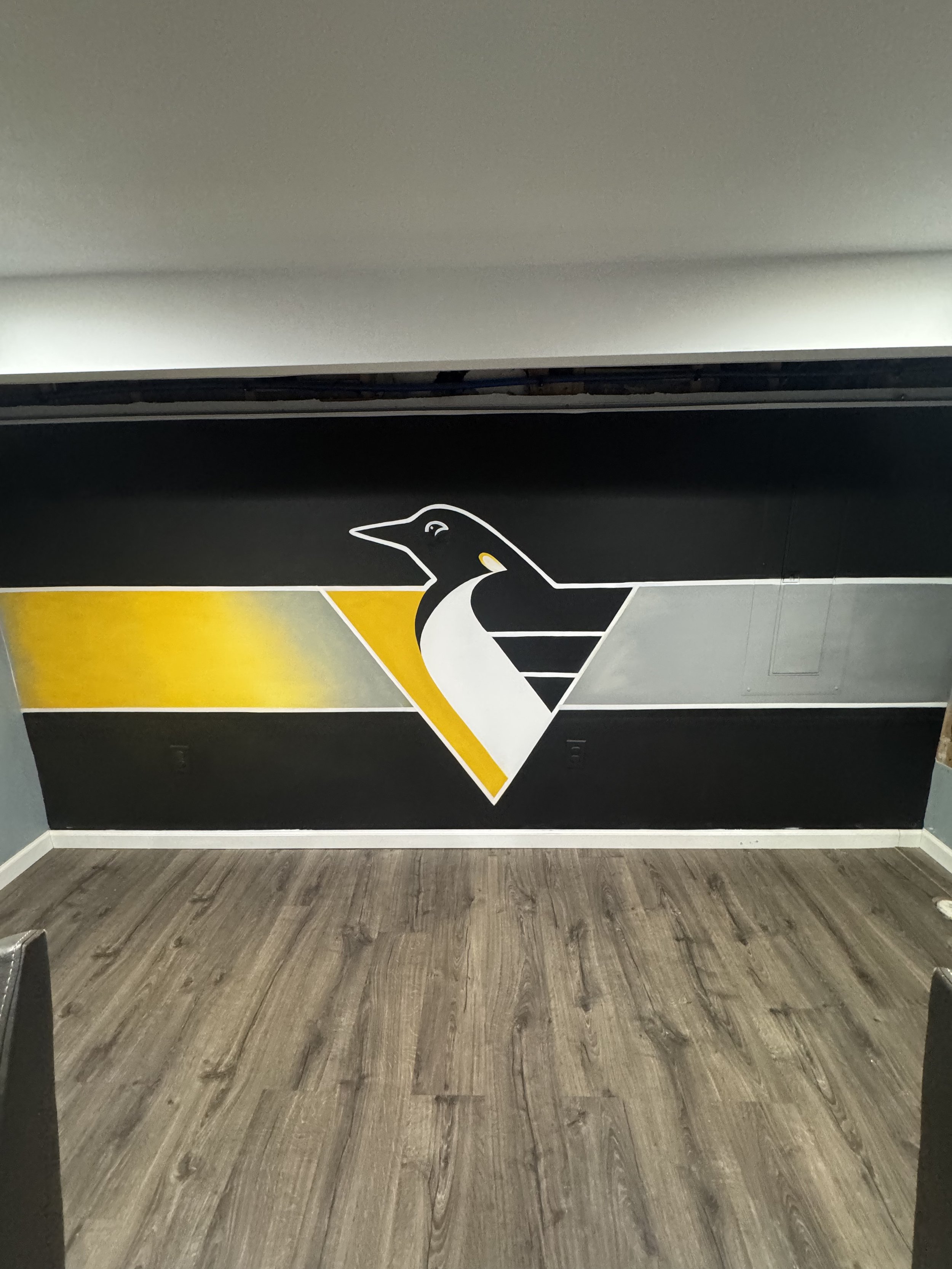 Wall with a large penguin graphic and yellow geometric design, brown wooden floor, gray wall