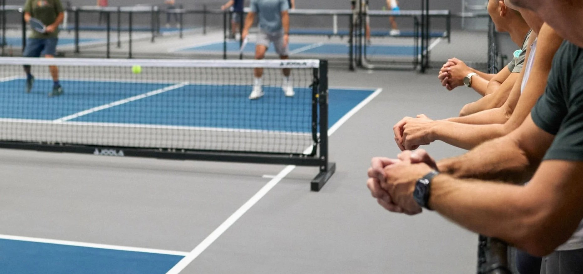 People watching a pickleball game from the sidelines of the court.