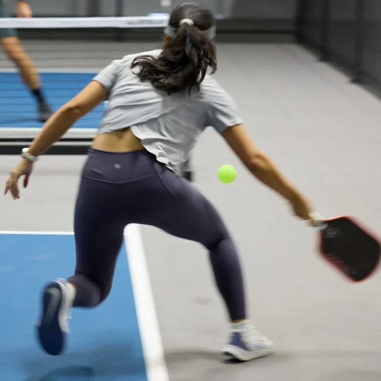 A woman playing pickleball indoors, hitting a bright green ball with a paddle, wearing athletic gear.