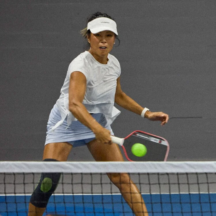 A female tennis player wearing a white sports outfit and visor hitting a green tennis ball with her racket during a match.